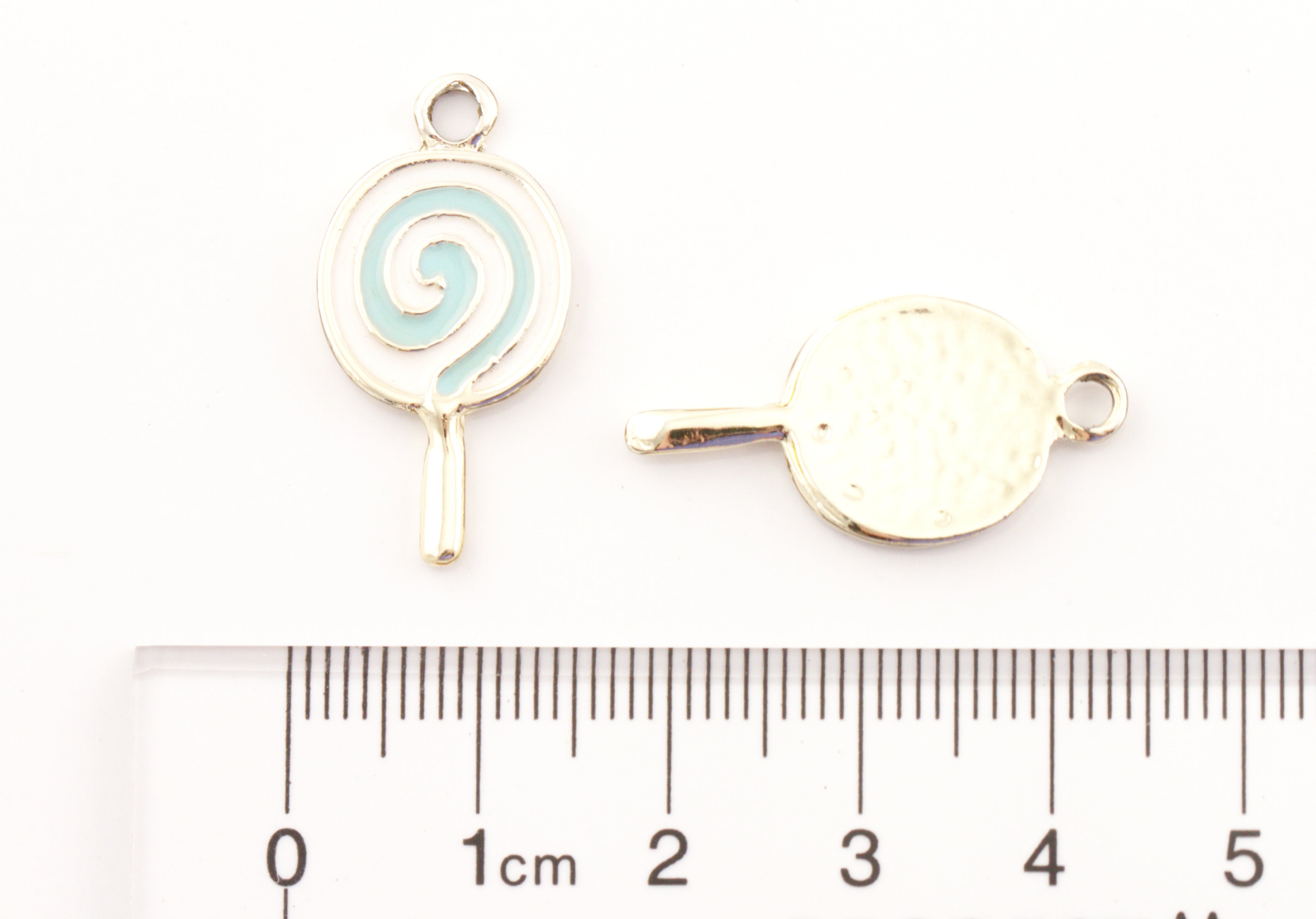 Two blue and white lollipop charms shown on a white background with a ruler at the bottom for scale. 