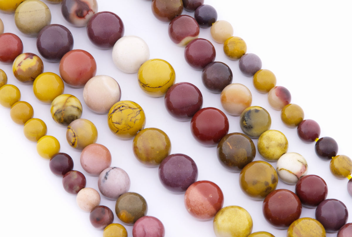Multiple strands of polished round mookaite gemstone beads in assorted earthy colors including yellow, burgundy, cream, pink, and brown, arranged diagonally on a white background.