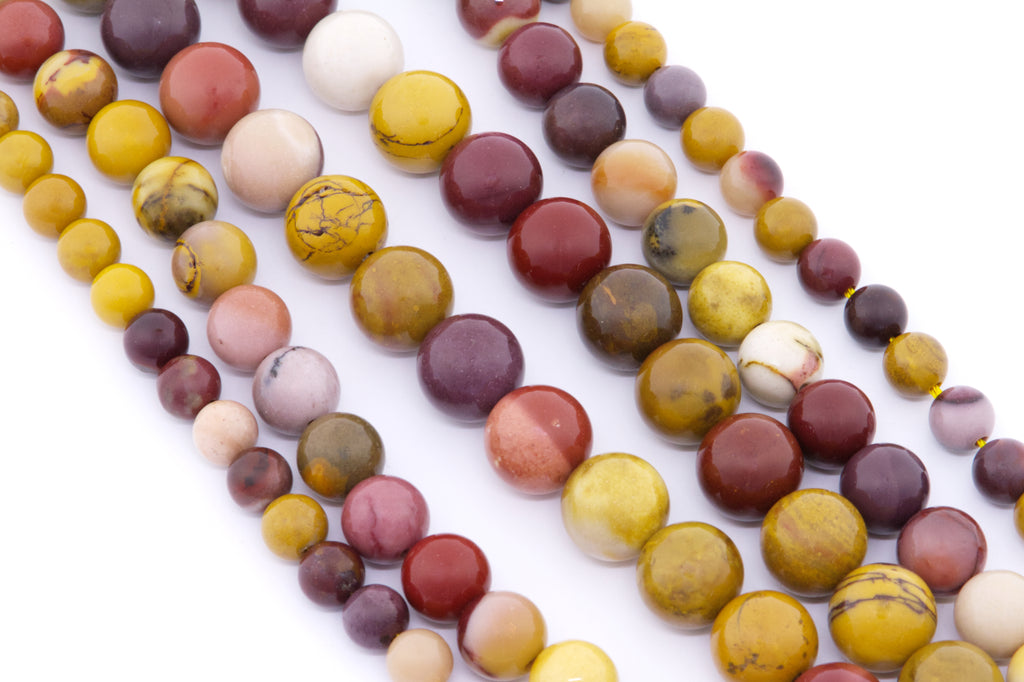 Multiple strands of polished round mookaite gemstone beads in assorted earthy colors including yellow, burgundy, cream, pink, and brown, arranged diagonally on a white background.