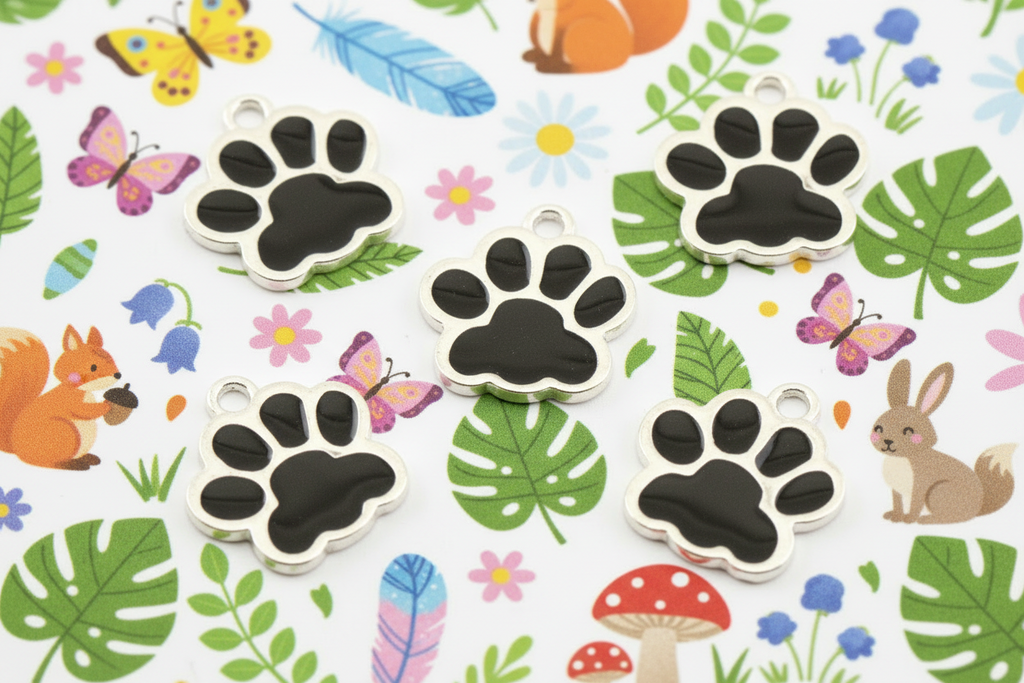 Five silver paw print charms with black centers are arranged on a white background decorated with colorful cartoon animals, leaves, and flowers.