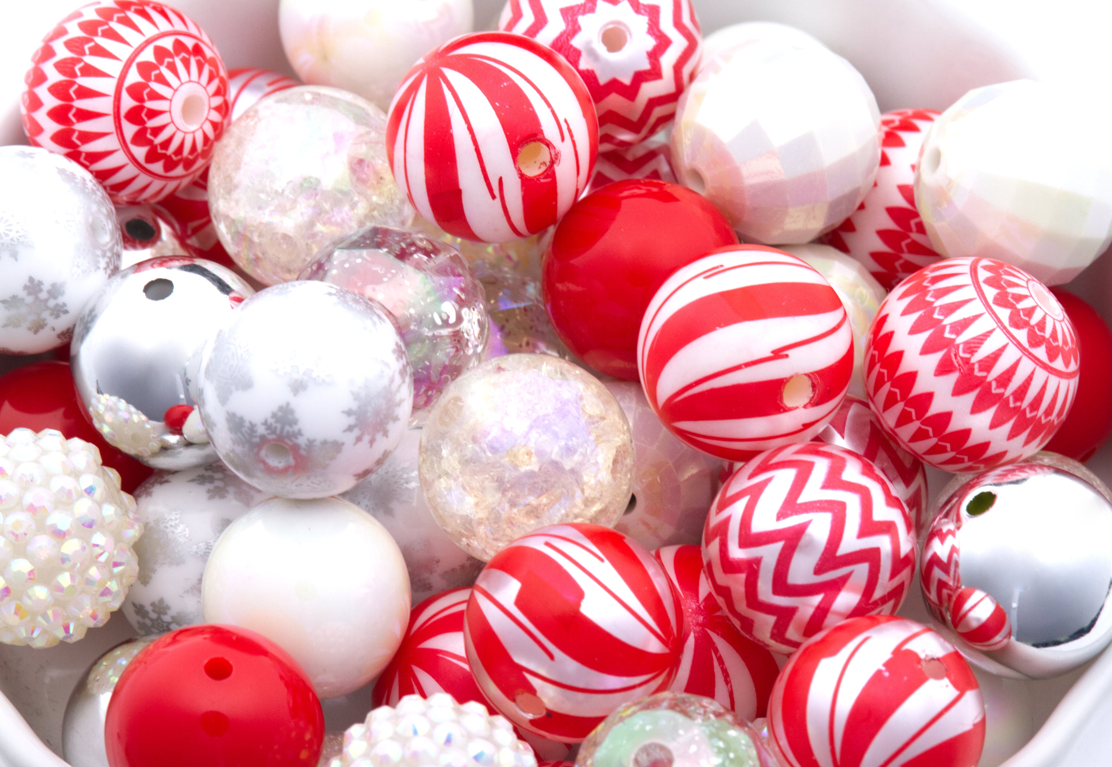 A close-up of assorted Christmas beads in a white bowl, featuring red, white, and silver holiday beads with striped, chevron, glitter, and textured finishes.
