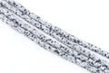 Several strands of polymer clay beads with a black and white pixelated or digital camouflage pattern, arranged diagonally on a plain white background.