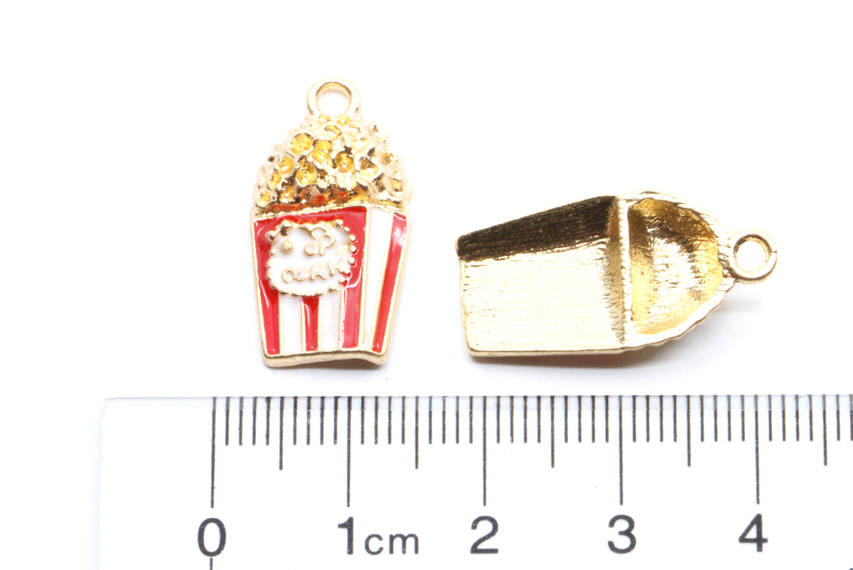 Two gold-tone popcorn-themed jewelry charms, one filled with red and white striped enamel and the other showing the reverse side, displayed above a cm ruler for scale on a white background.