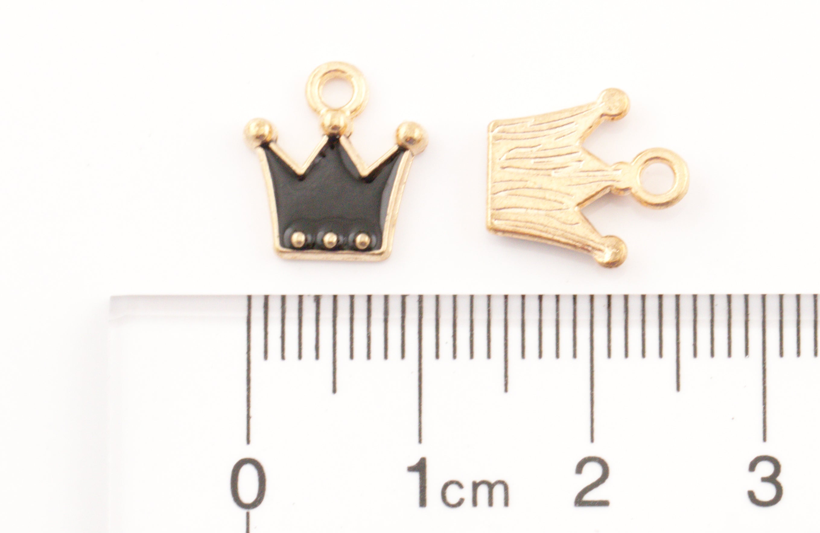 Two small crown-shaped jewelry charms shown above a ruler for scale on a white background. 