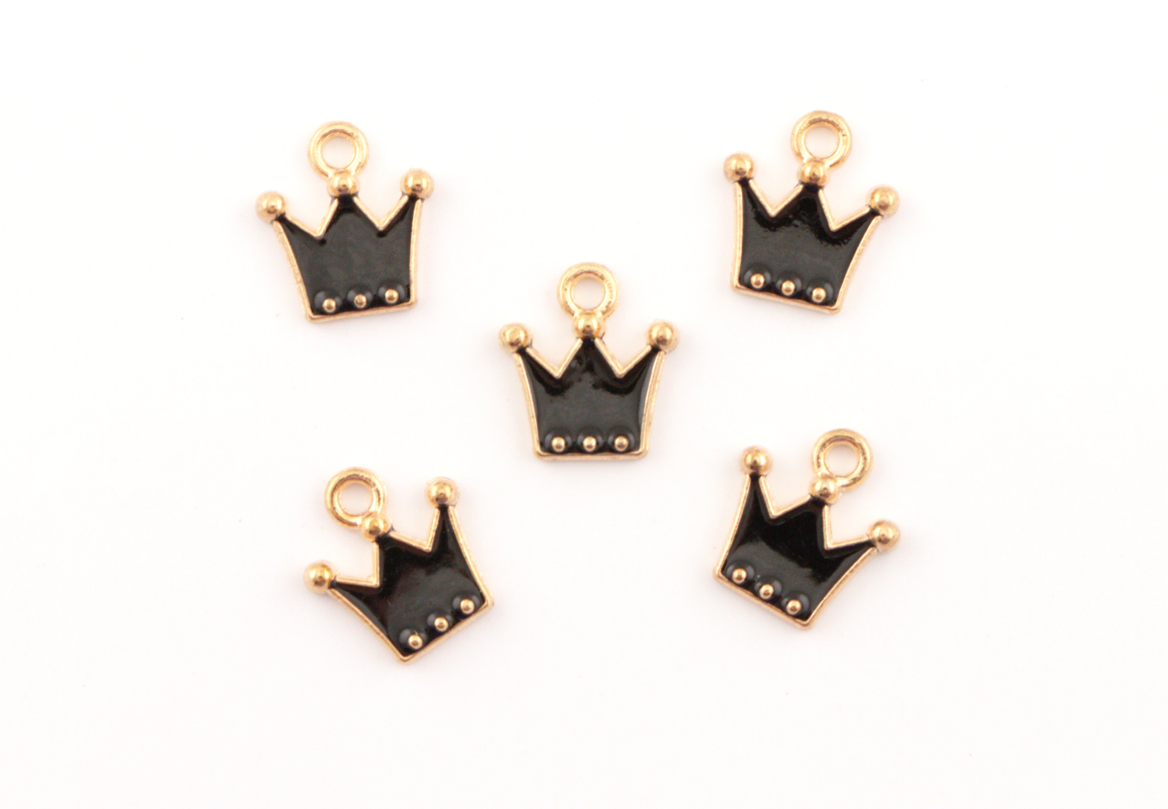 Five small crown-shaped charms with black enamel and gold-tone metal borders, arranged on a plain white background.