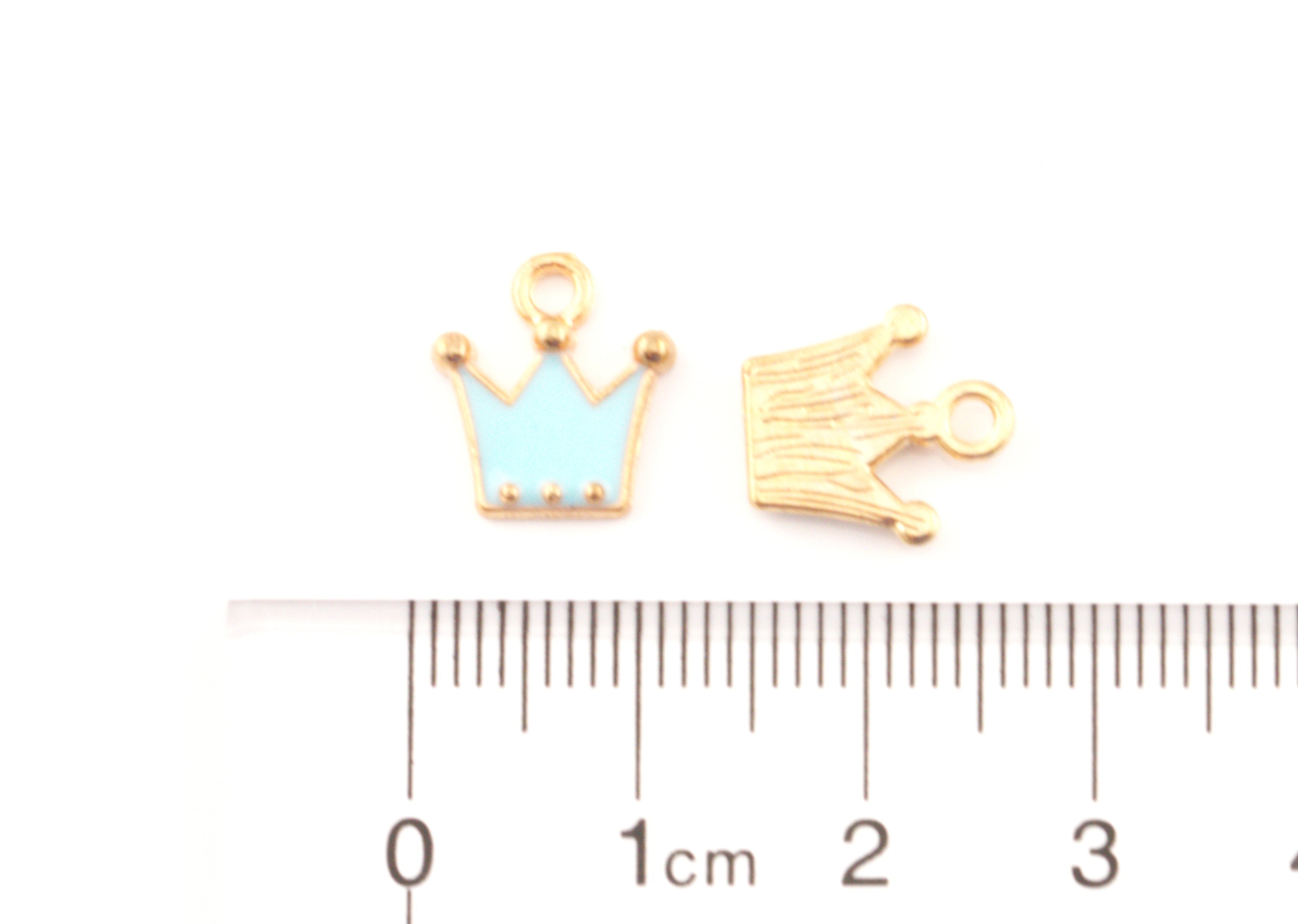 Two small crown-shaped jewelry charms,  shown above a cm ruler for scale on a white background.