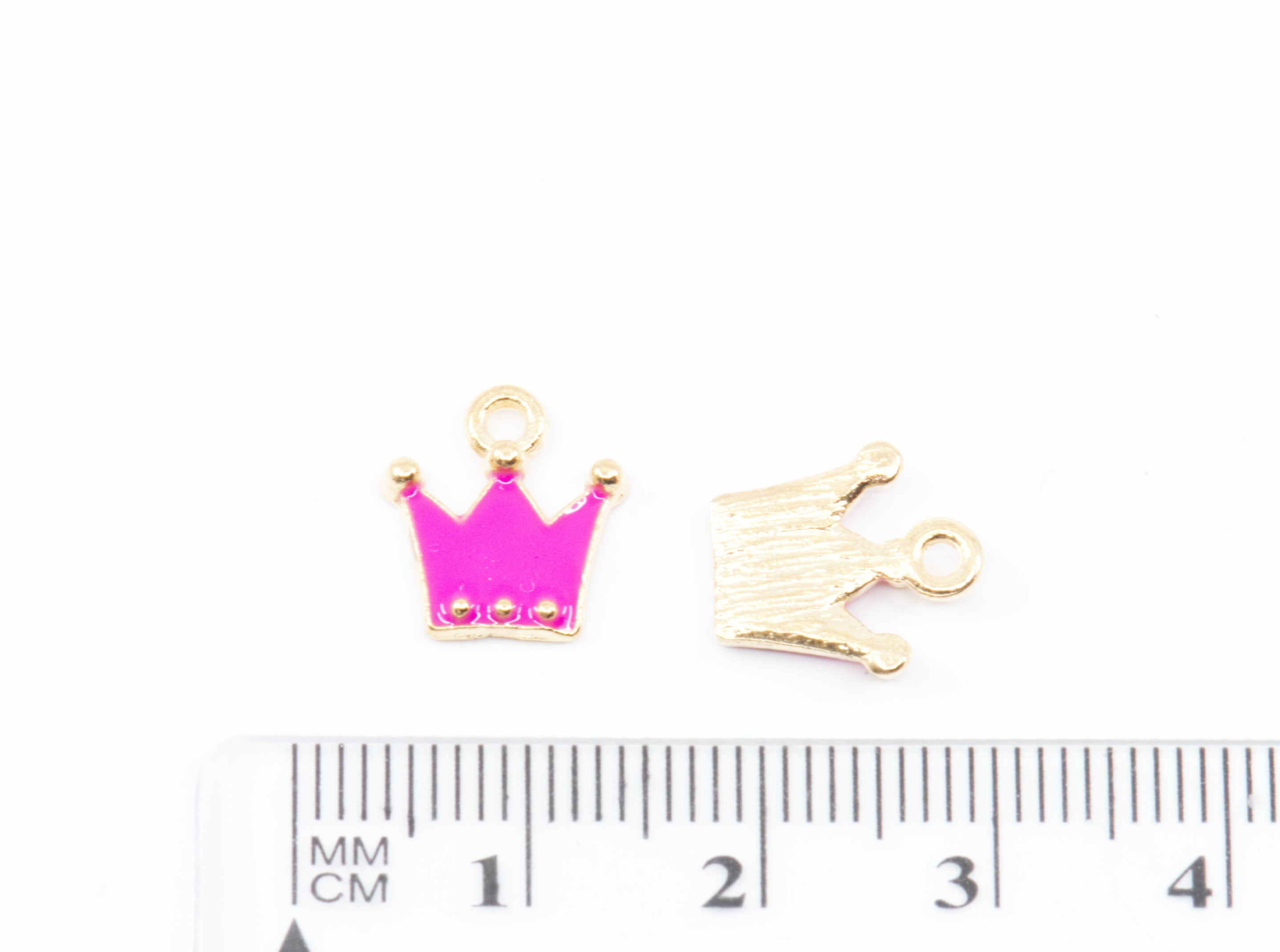 Two small crown-shaped jewelry charms shown above a ruler for scale on a white background.