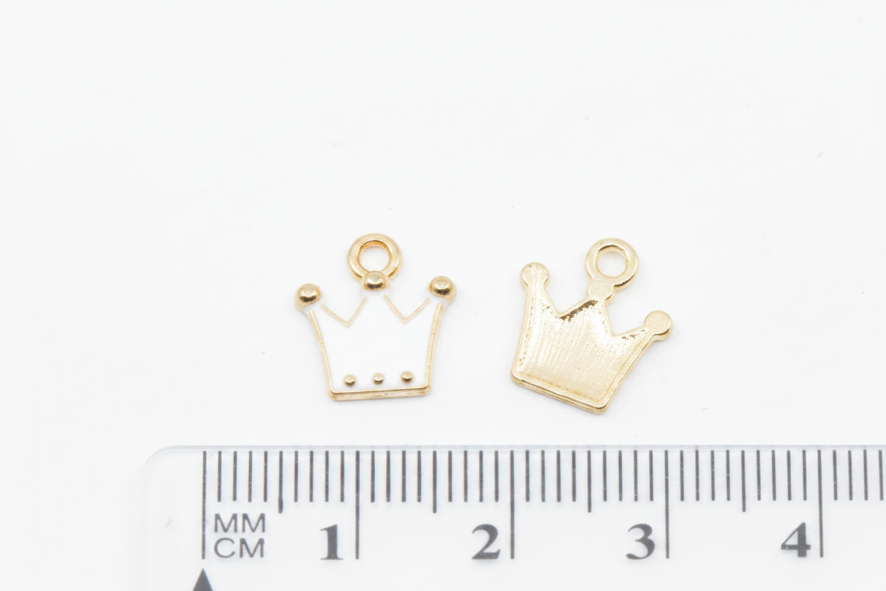 Two small gold crown-shaped jewelry findings or charms shown on a white background with a ruler at the bottom for scale.