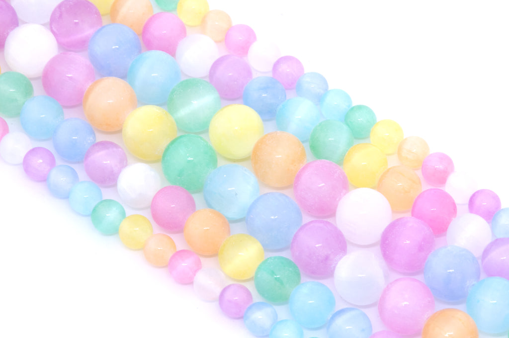 A close-up of multiple strands of pastel rainbow dyed gypsum selenite beads arranged diagonally on a white background.