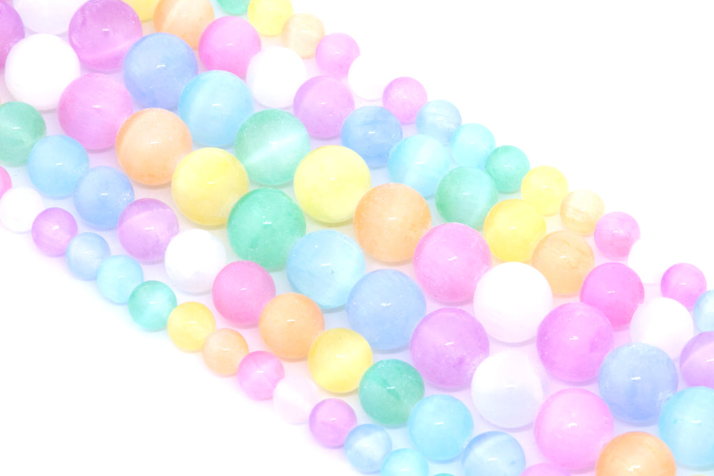 A close-up of multiple strands of pastel rainbow dyed gypsum selenite beads arranged diagonally on a white background.