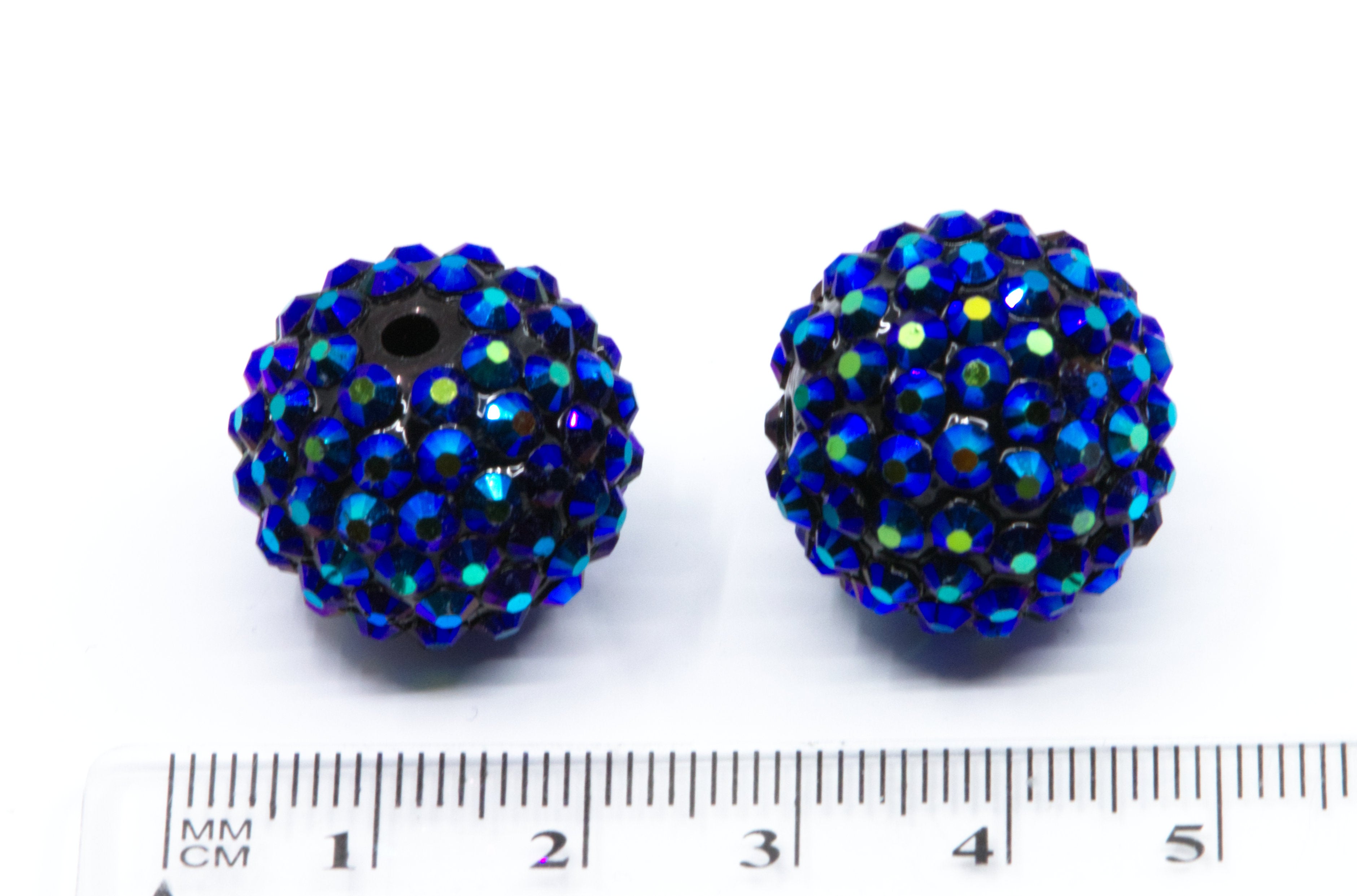 Two round metallic blue rhinestone beads with a black base, shown next to a  cm ruler for scale on a white background.