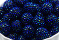 A close-up of multiple metallic blue rhinestone covered beads piled in a white container.