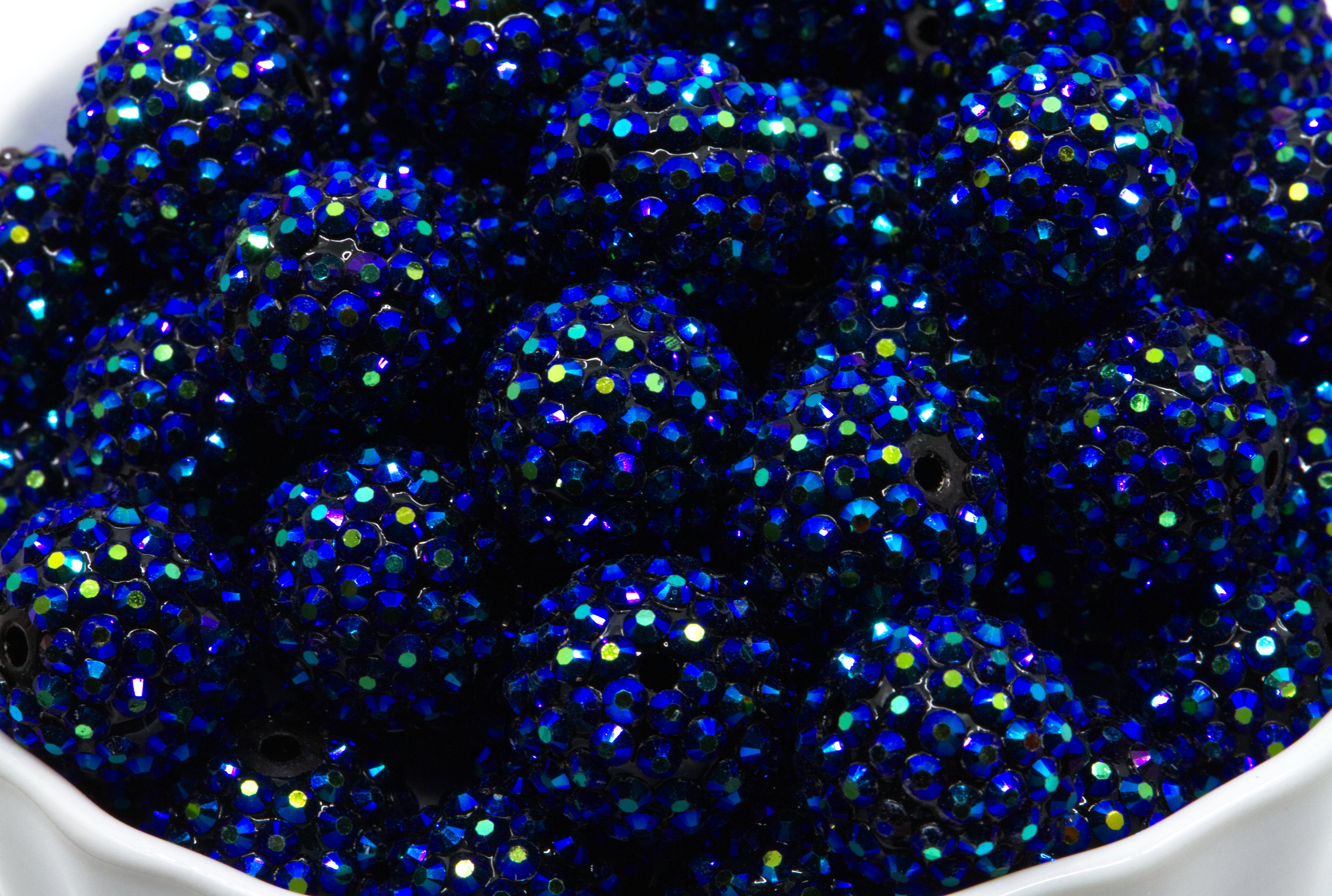 A close-up of multiple metallic blue rhinestone covered beads piled in a white container.