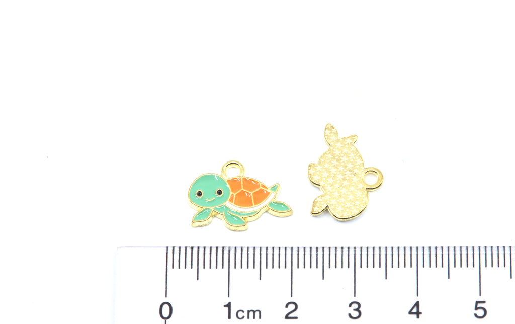 Two small turtle-shaped jewelry charms on a white background above a ruler for scale. 