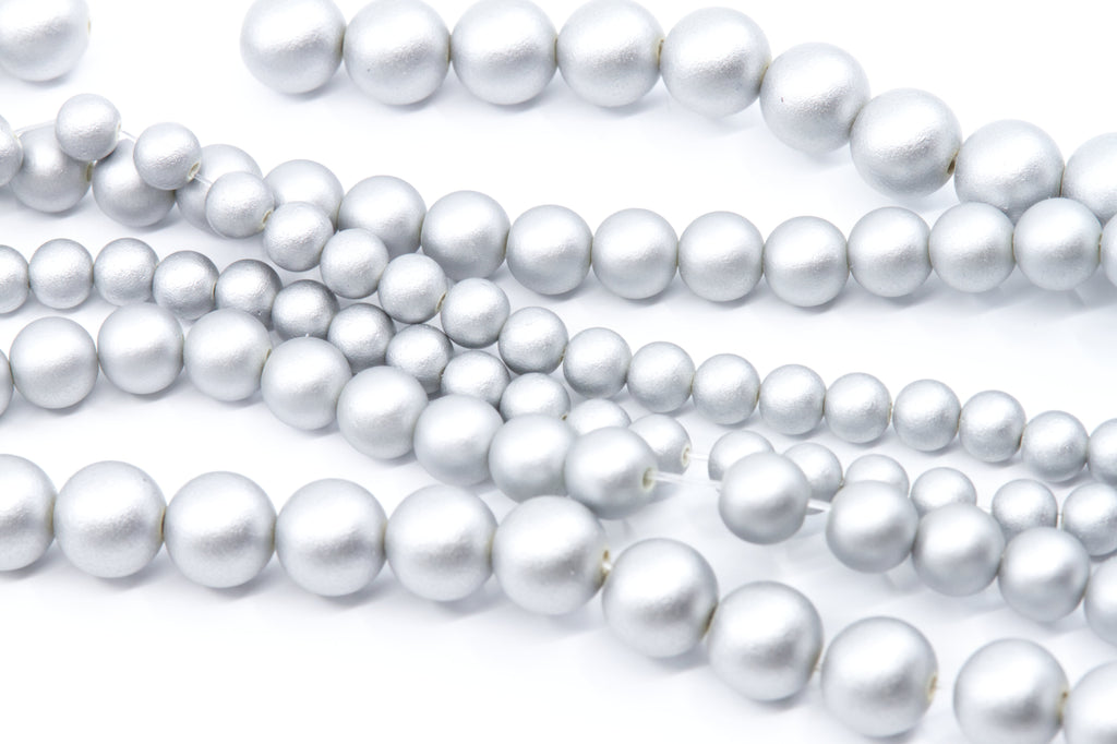 Multiple strands of silver shimmery acrylic beads in various sizes, arranged diagonally on a clean white background.