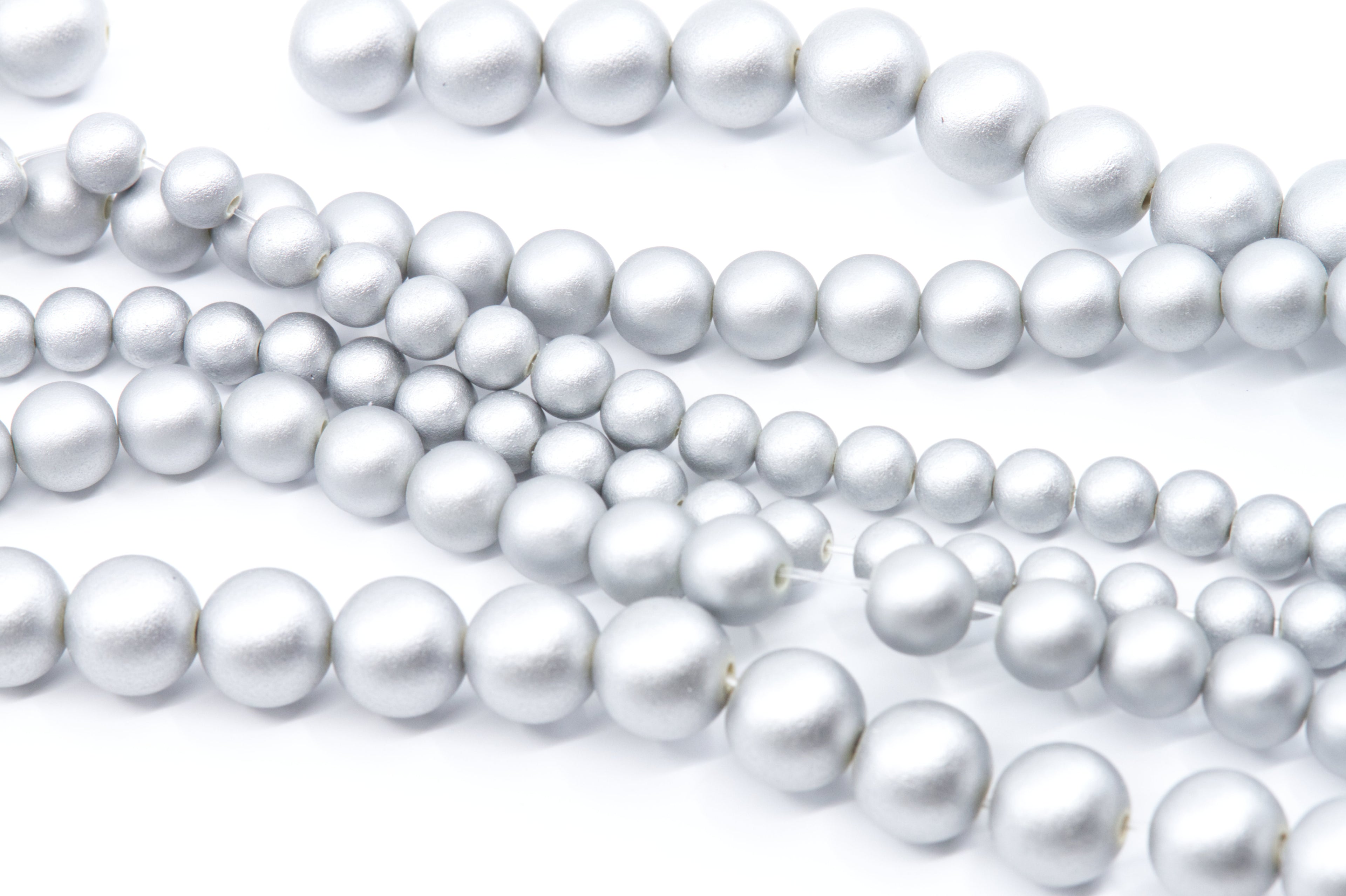 Multiple strands of silver shimmery acrylic beads in various sizes, arranged diagonally on a clean white background.