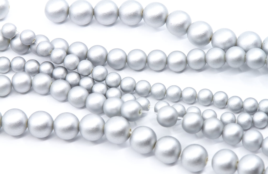 Multiple strands of silver shimmery acrylic beads in various sizes, arranged diagonally on a clean white background.