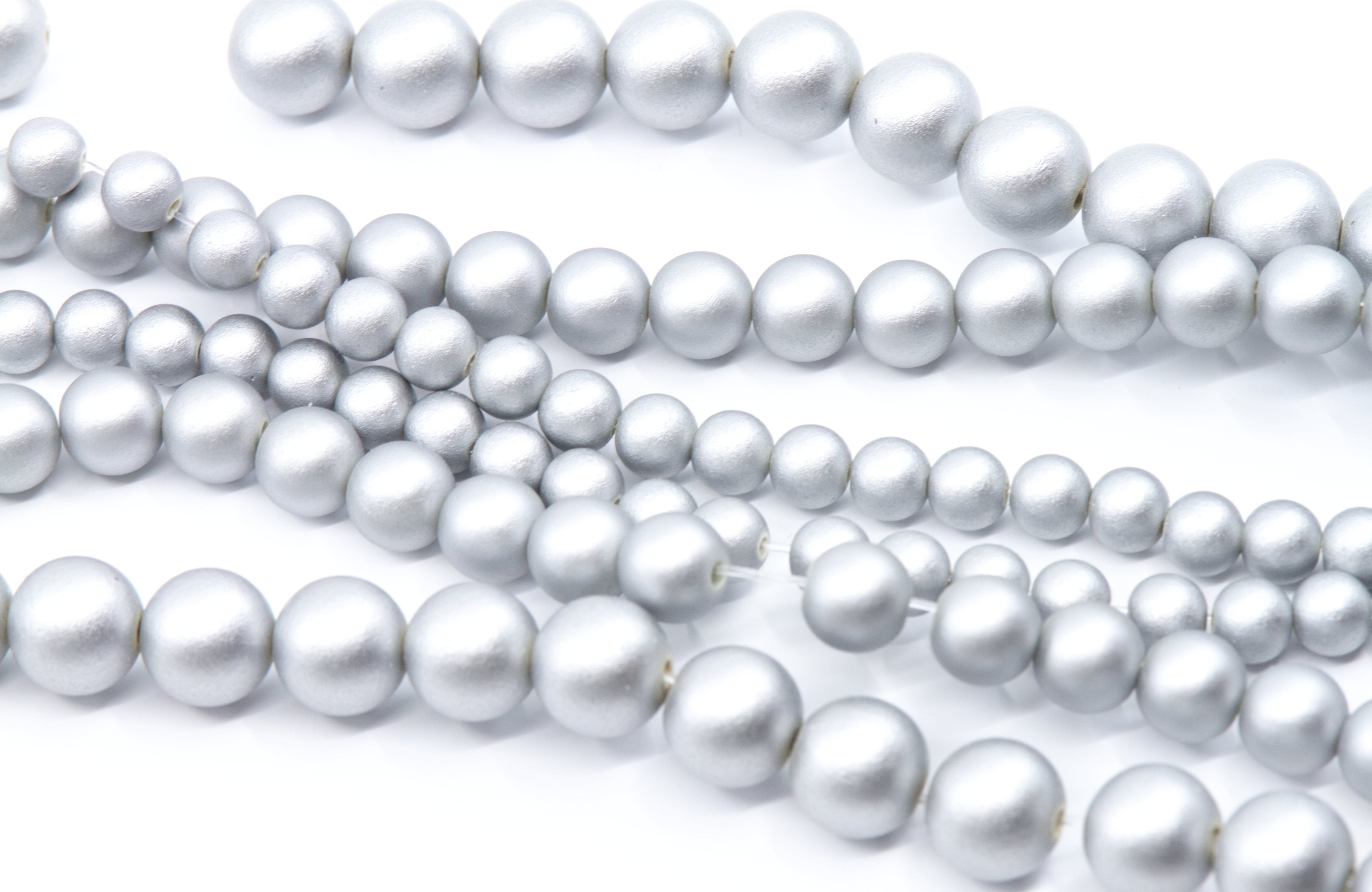 Multiple strands of silver shimmery acrylic beads in various sizes, arranged diagonally on a clean white background.