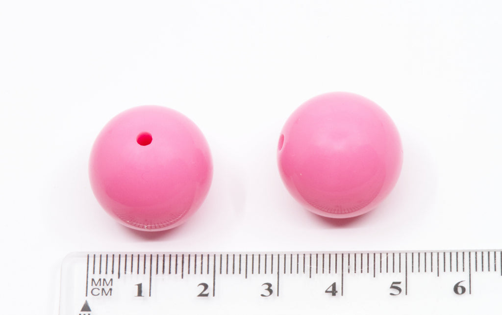 Two pink beads with a ruler for scale on a white background