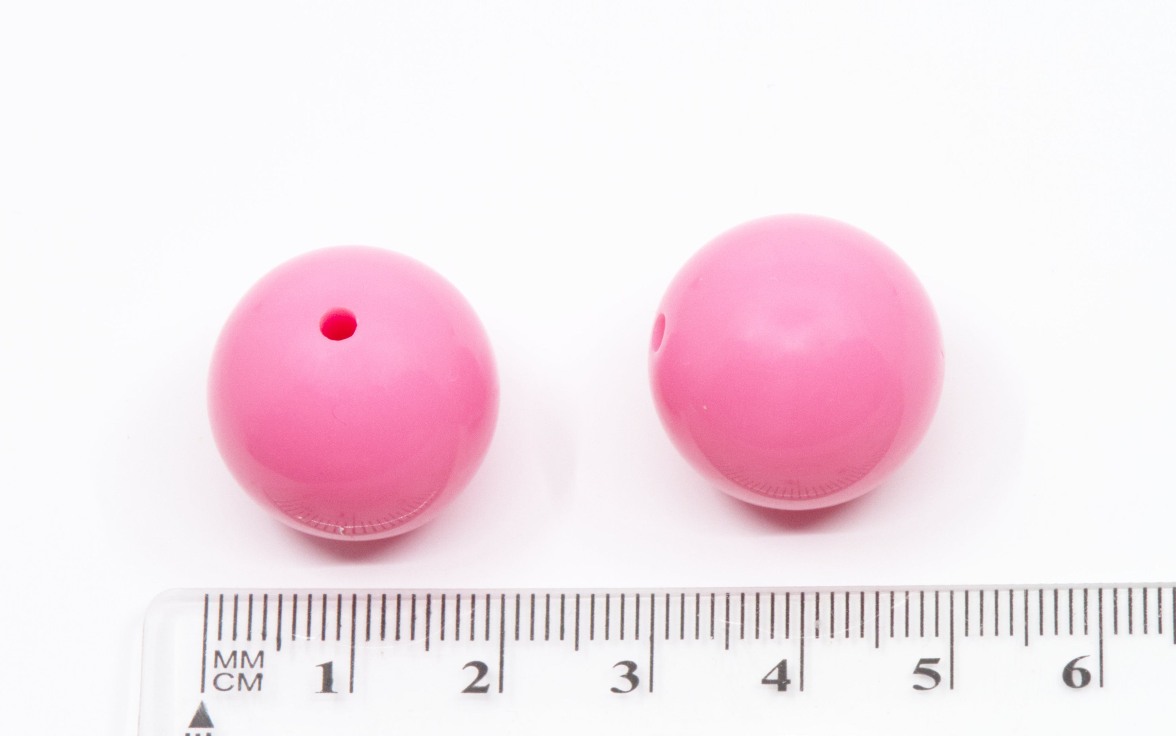Two pink beads with a ruler for scale on a white background