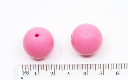 Two pink beads with a ruler for scale on a white background