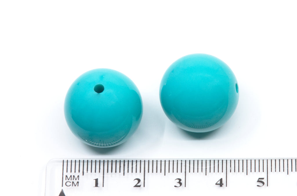 Two blue beads with a ruler for scale on a white background