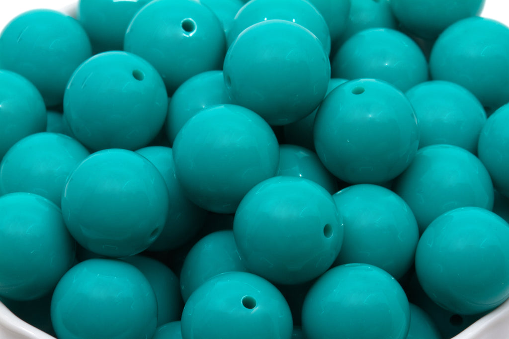 teal beads in a white bowl on white background