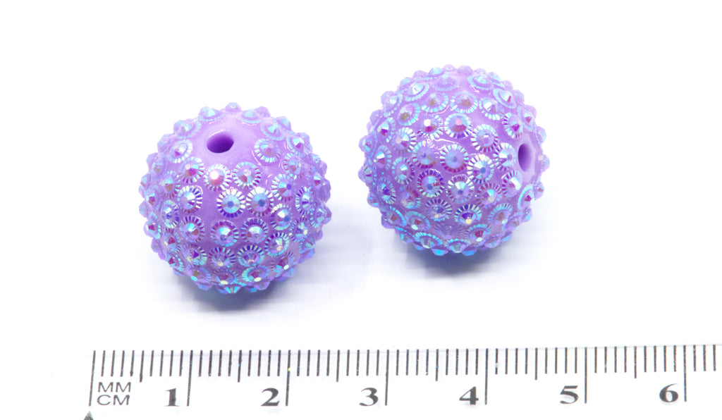 Two purple sunburst rhinestone beads, shown next to a cm ruler on a white background.