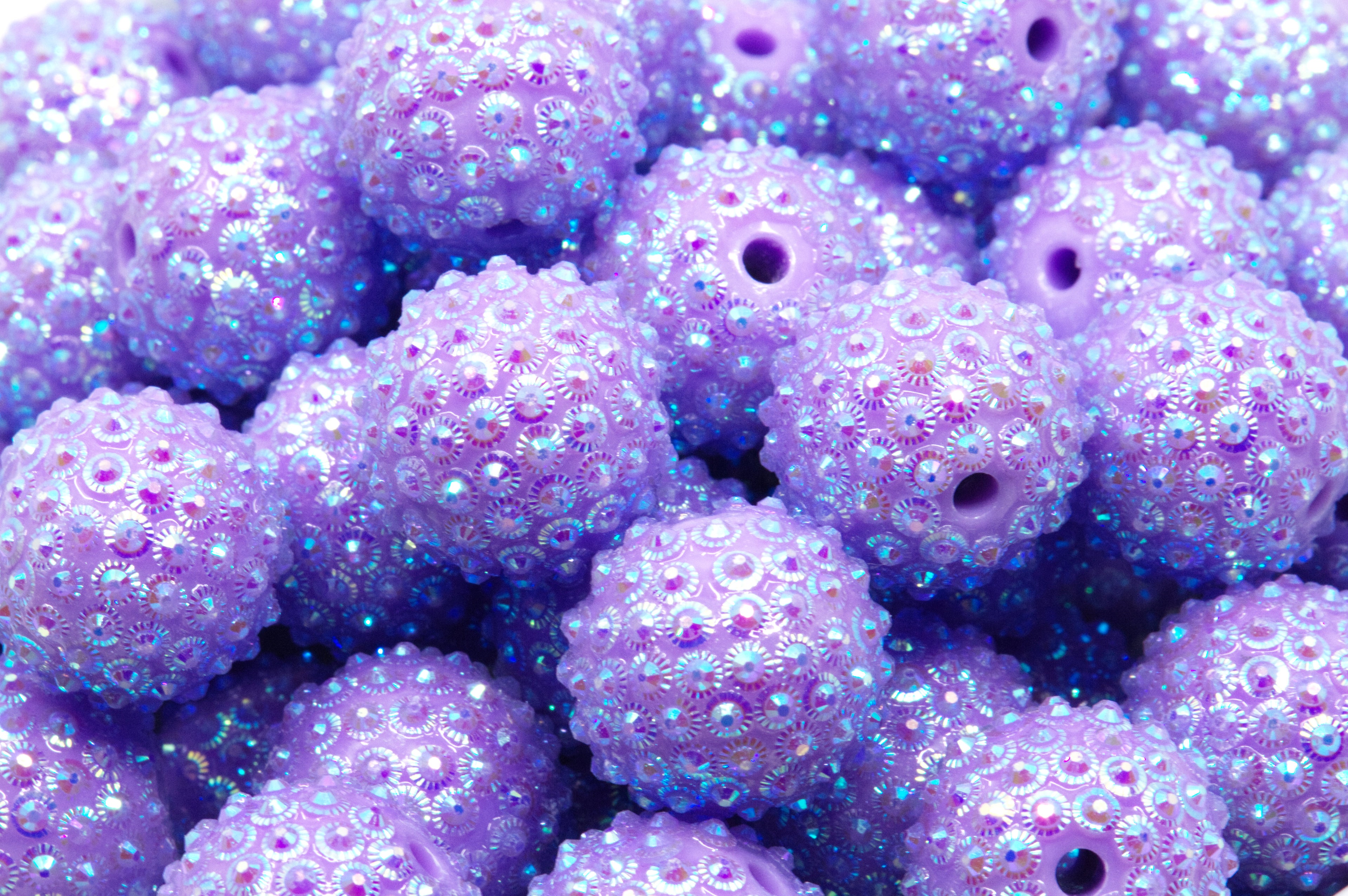 A close-up pile of purple sunburst rhinestone beads in a white bowl on a white background. 
