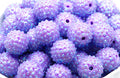 A close-up pile of purple sunburst rhinestone beads in a white bowl on a white background. 