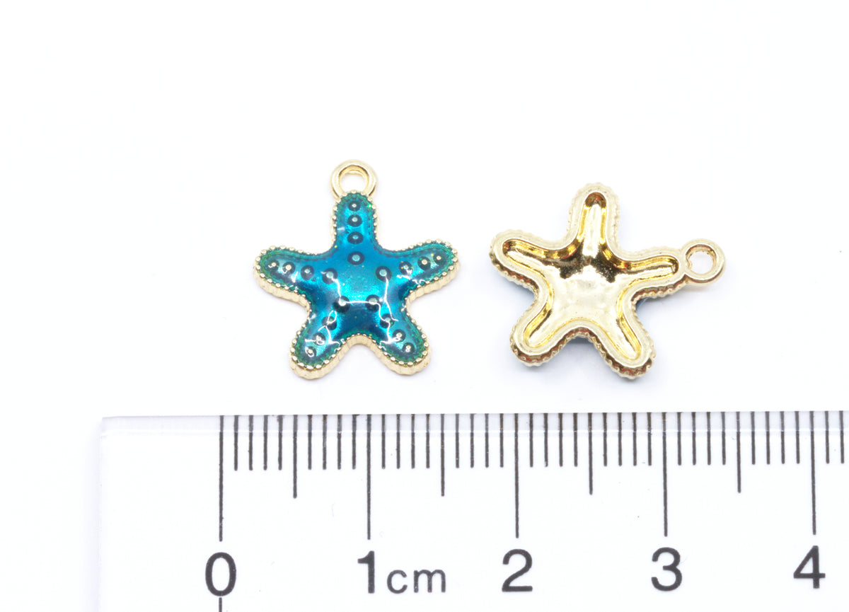 Two small starfish-shaped jewelry charms  shown on a white background above a ruler for scale.