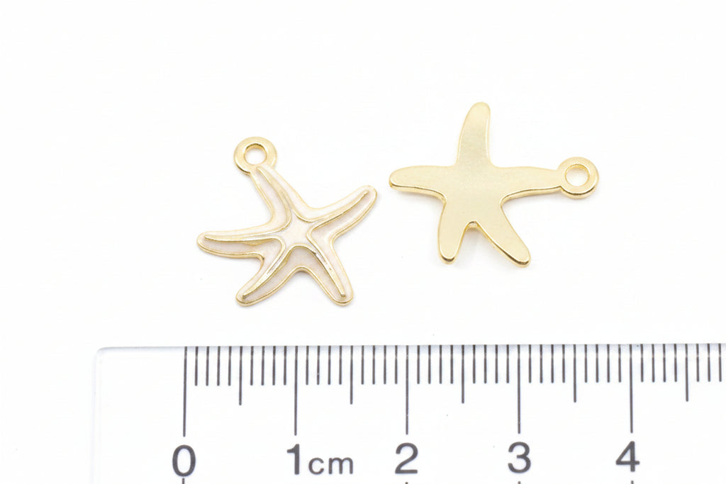 Two small gold starfish-shaped jewelry charms shown above a ruler on a white background.