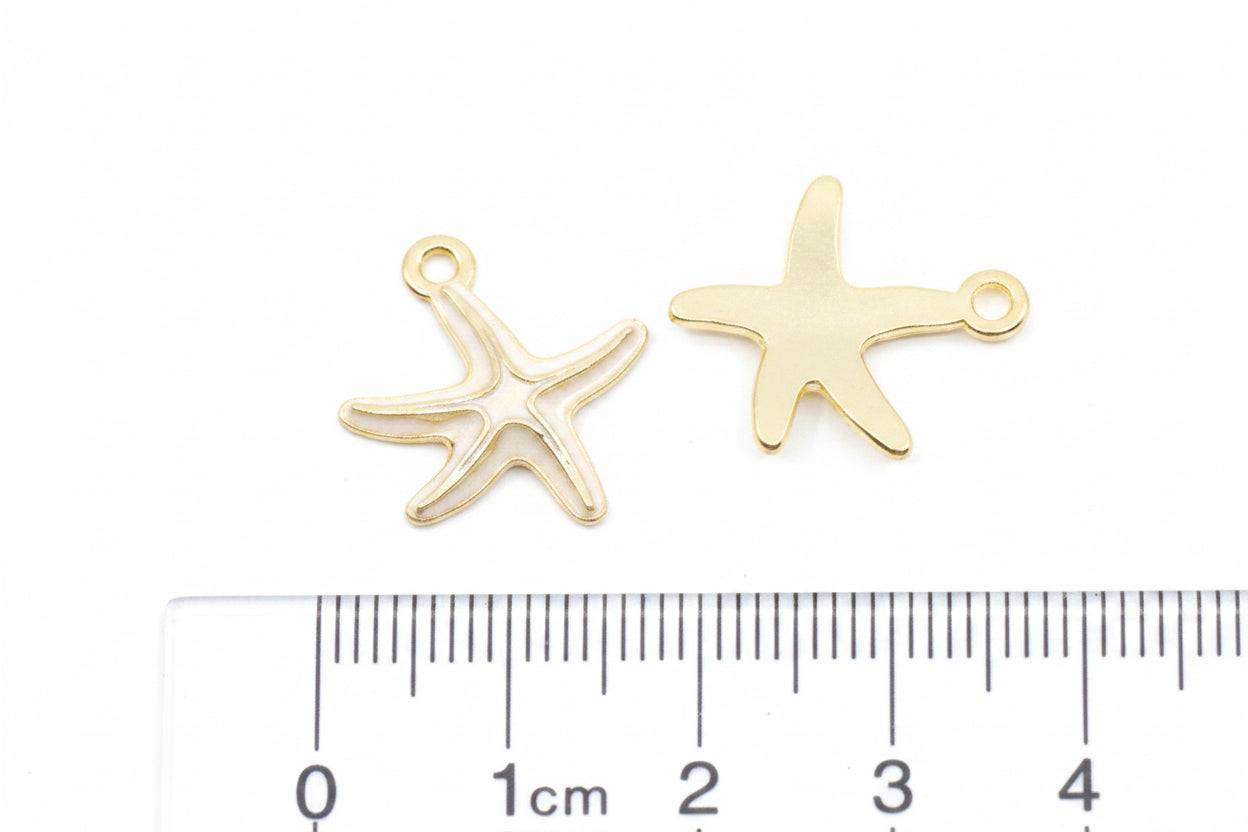 Two small gold starfish-shaped jewelry charms shown above a ruler on a white background.