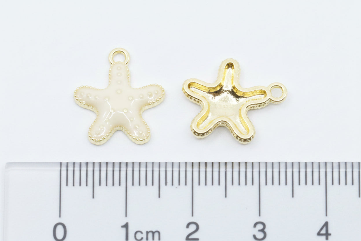 Two small starfish-shaped jewelry charms, displayed above a  cm ruler for scale on a white background.