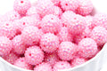 A close-up of pink rhinestone bubblegum beads, piled in a white bowl against a white background.