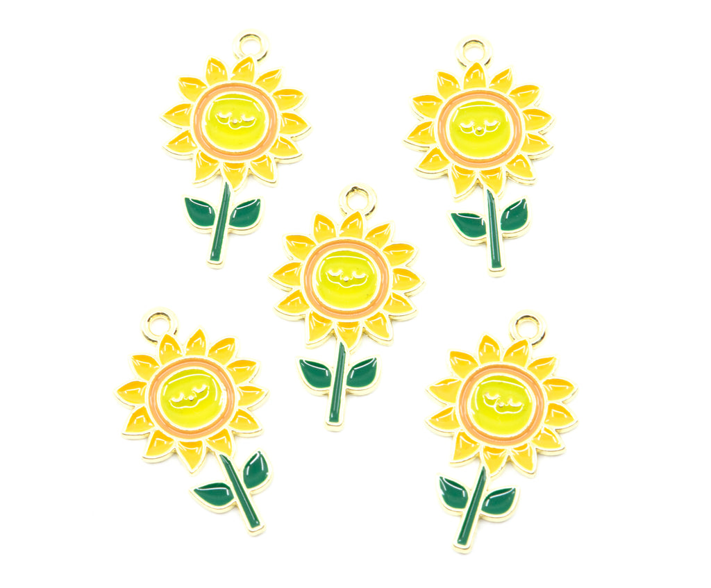 Five enamel sunflower charms with gold-tone metal edges, yellow petals, green stems and leaves, and smiling yellow flower centers, arranged on a plain white background.