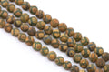 A close-up of multiple strands of round Tibetan agate beads in brown and green with a frosted surface , arranged diagonally on a plain white background.