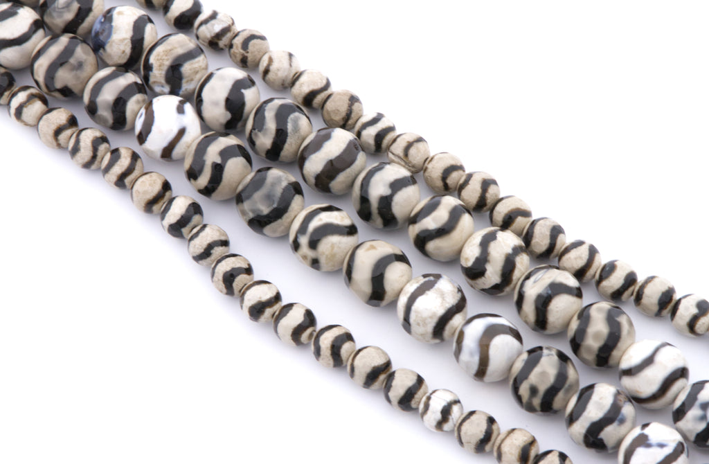 Four strands of round zebra striped beads with black and off-white stripes, arranged diagonally on a white background.