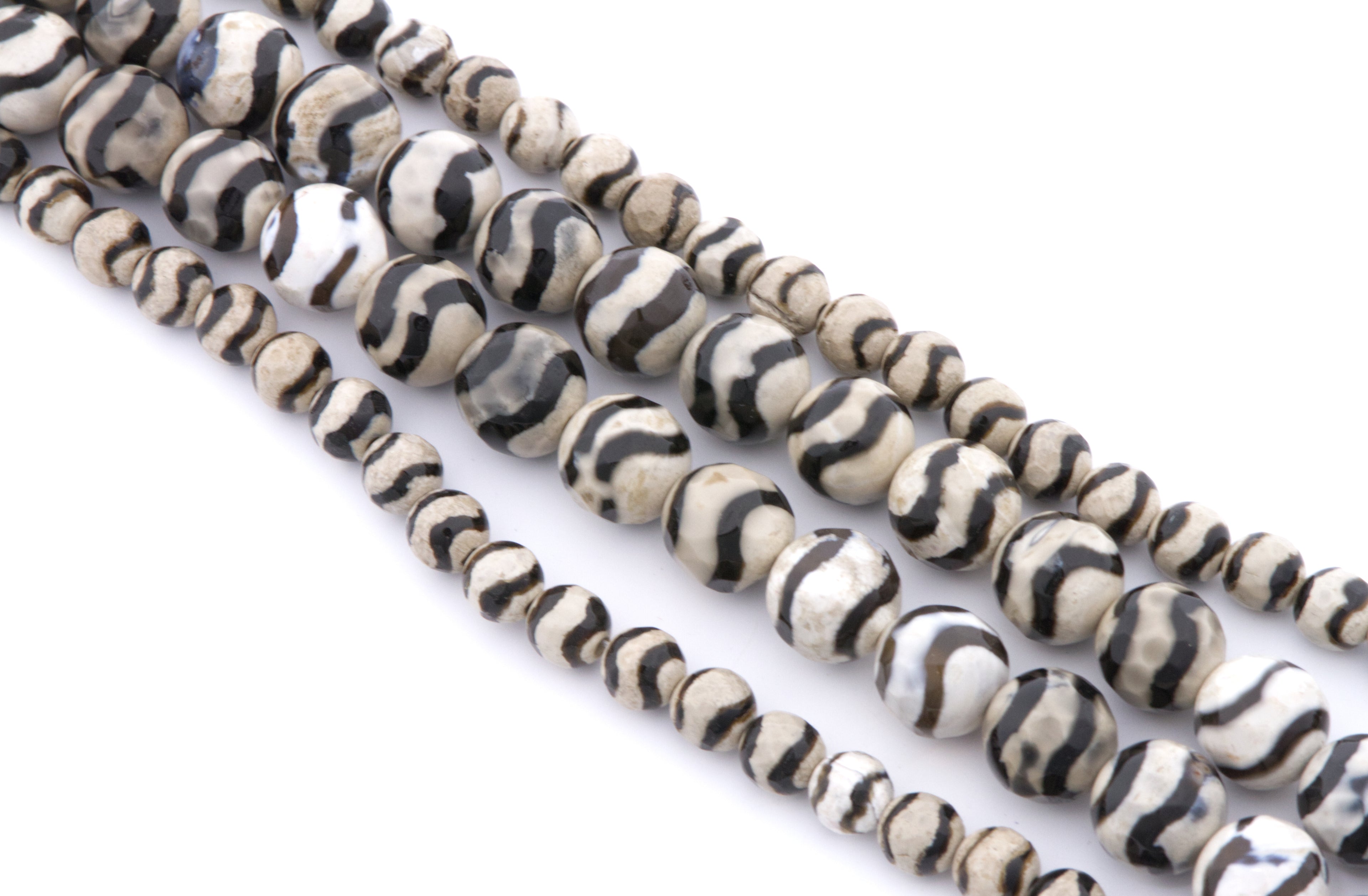 Four strands of round zebra striped beads with black and off-white stripes, arranged diagonally on a white background.