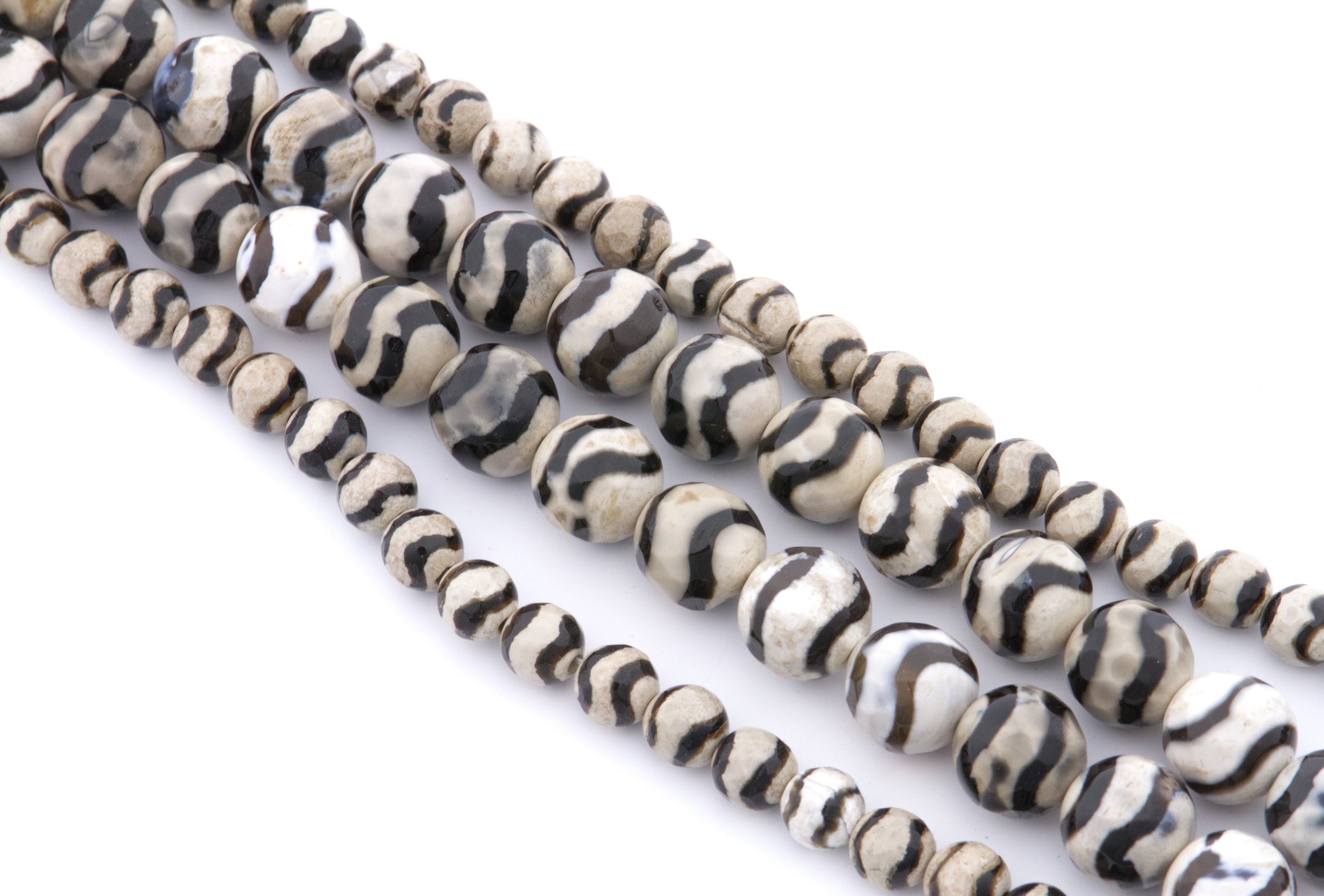 Four strands of round zebra striped beads with black and off-white stripes, arranged diagonally on a white background.