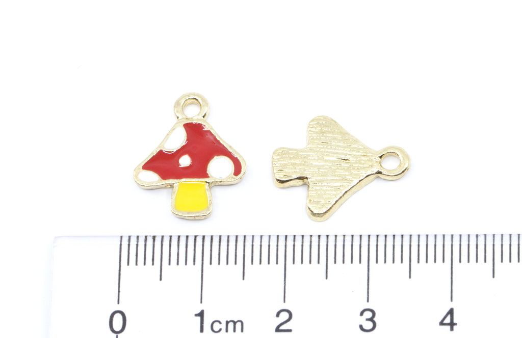 Two small red, yellow and white mushroom jewelry charms shown on a white background with a ruler at the bottom for scale.