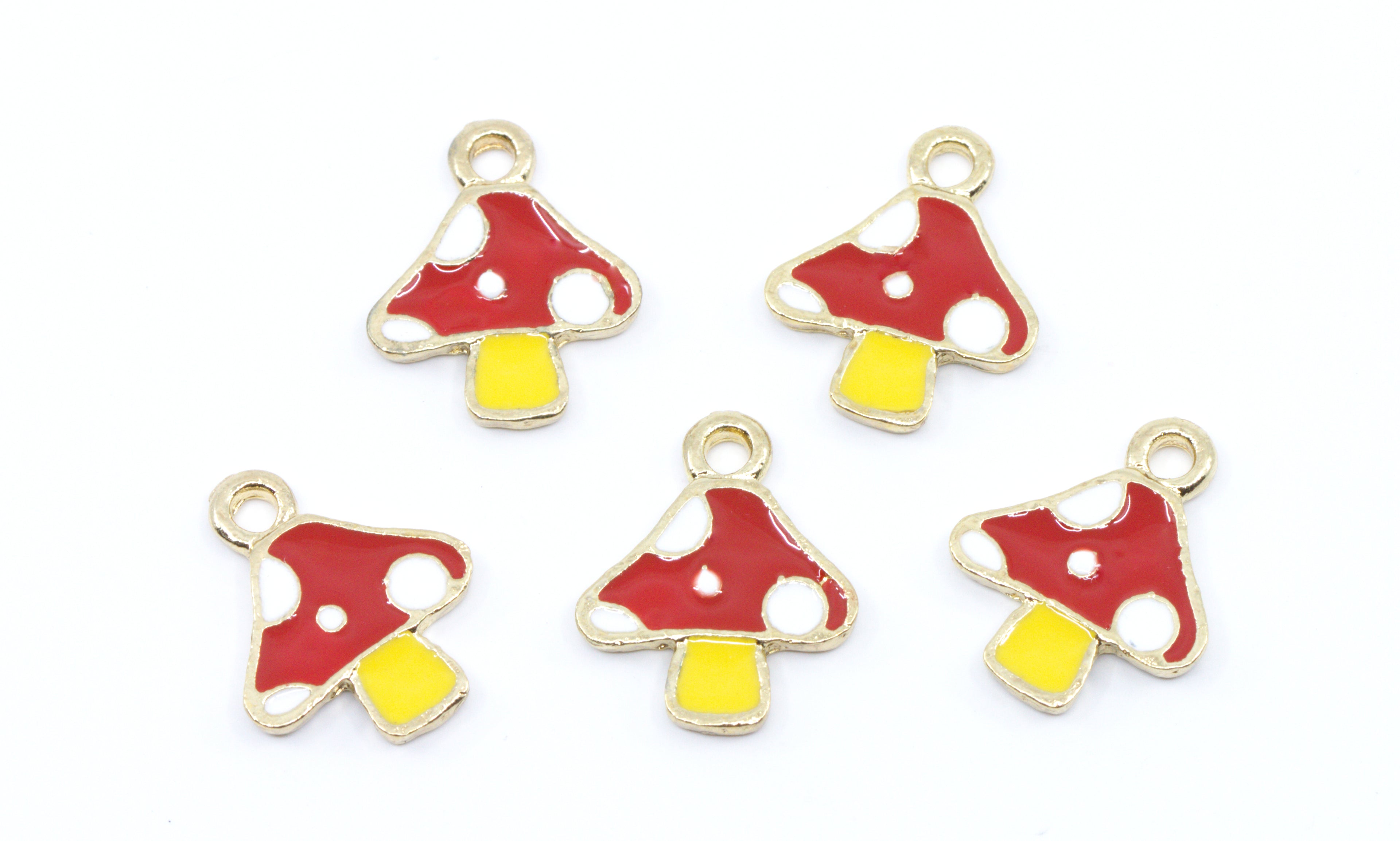 Five small mushroom-shaped charms with red and white spotted caps and yellow stems, outlined in gold-tone metal, arranged on a plain white background.