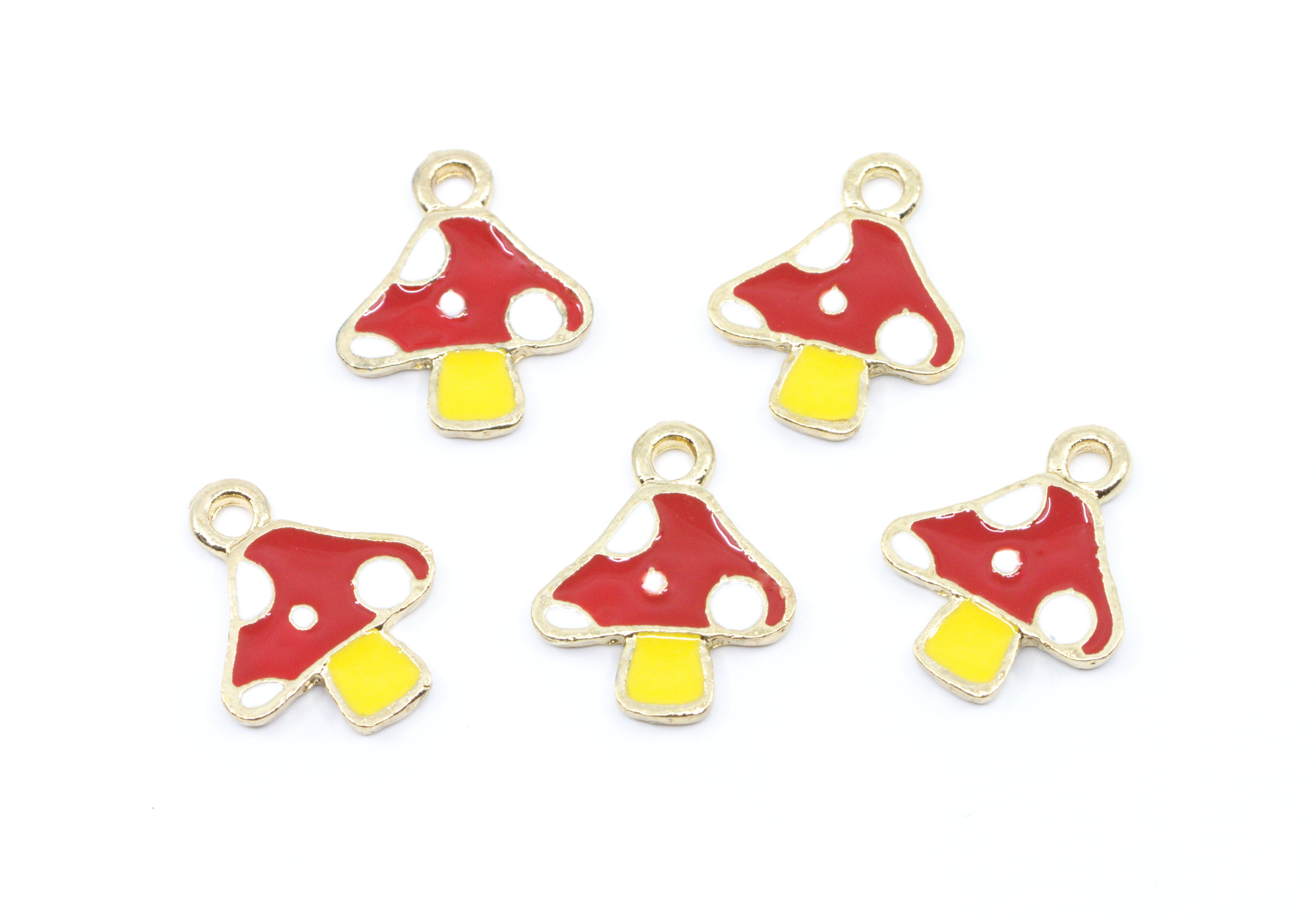 Five small mushroom-shaped charms with red and white spotted caps and yellow stems, outlined in gold-tone metal, arranged on a plain white background.