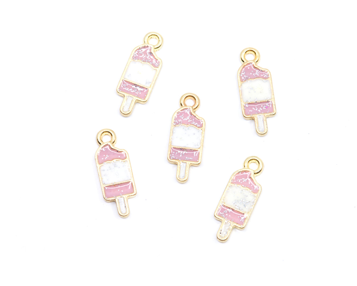 Five small ice cream bar-shaped jewelry charms with gold-tone metal outlines, featuring pink and white glittery enamel details, arranged on a plain white background.