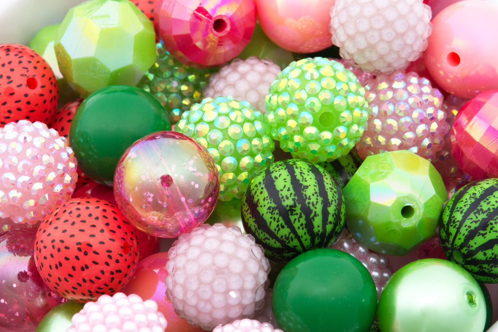 A close-up pile of colorful bubblegum beads with various patterns and textures, including watermelon print, faceted, iridescent rhinestones, and smooth glossy finishes.