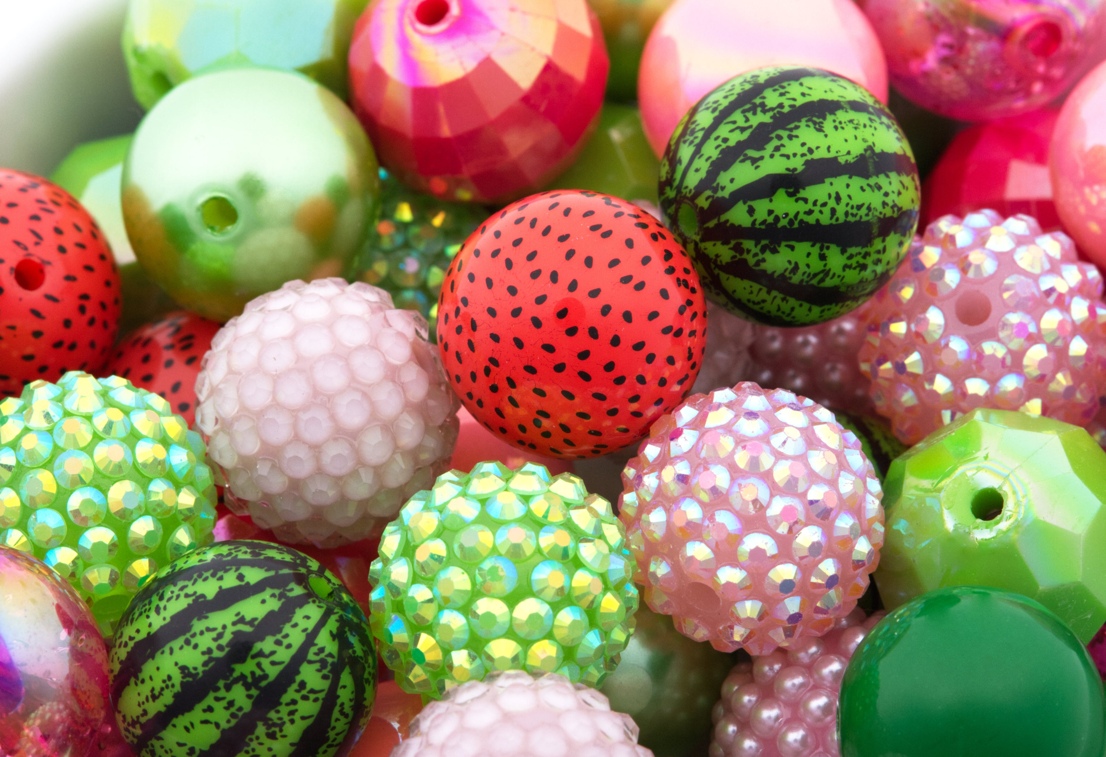 A close-up pile of colorful bubblegum beads with various patterns and textures, including watermelon print, faceted, iridescent rhinestones, and smooth glossy finishes.