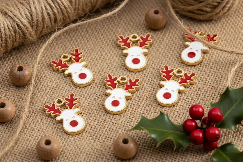 Six Christmas reindeer head charms with white enamel, red accents, and gold-tone metal details, arranged on a burlap surface with twine, wooden beads, and holly leaves and berries.