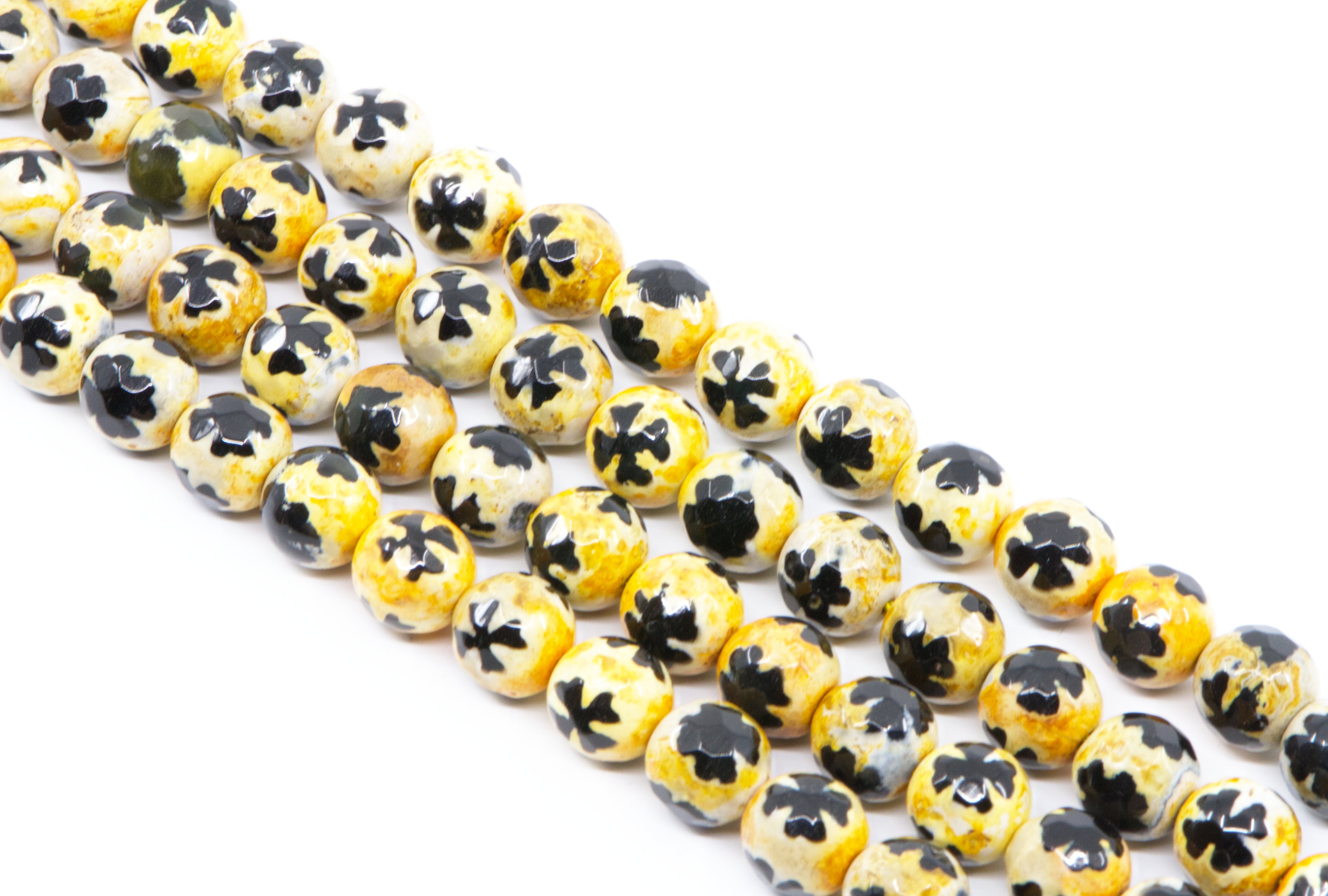 A close-up of a multiple strands of round beads with a yellow base and a blue clover-like pattern on top, arranged diagonally on a white background.