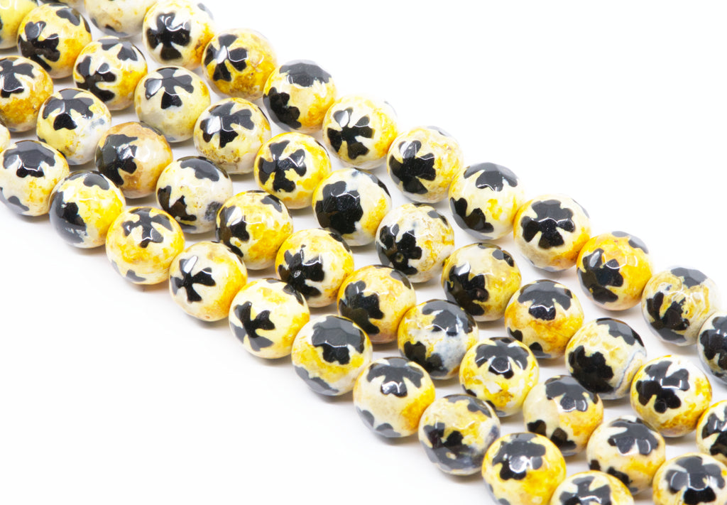 A close-up of a multiple strands of round beads with a yellow base and a blue clover-like pattern on top, arranged diagonally on a white background.