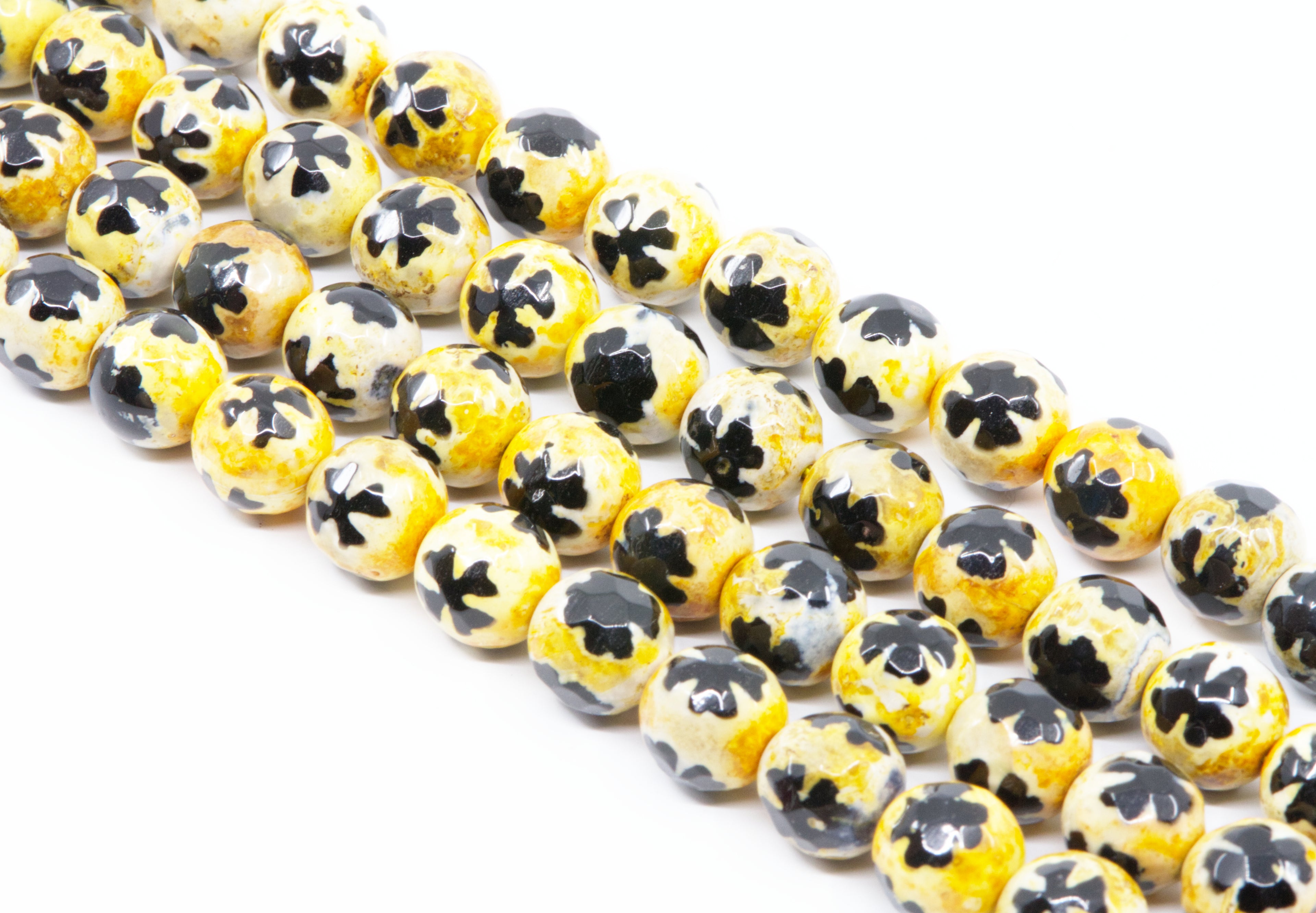 A close-up of a multiple strands of round beads with a yellow base and a blue clover-like pattern on top, arranged diagonally on a white background.